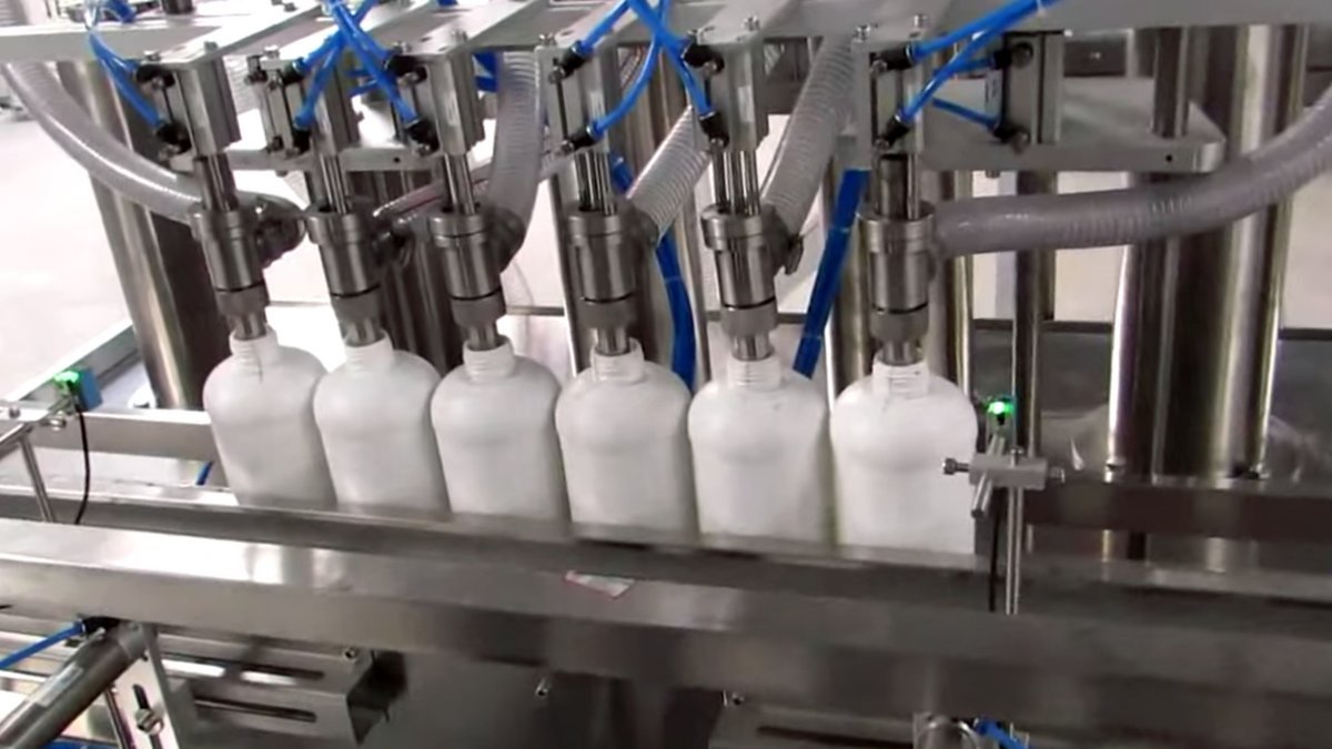 Automated multi-head liquid detergent filling and bottle capping conveyor line in a manufacturing plant