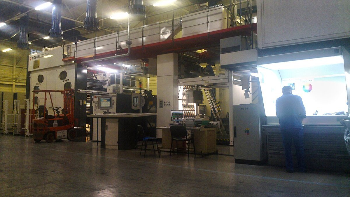 Industrial flexographic packaging printing press showing doctor blade ink chamber and active color web in operation