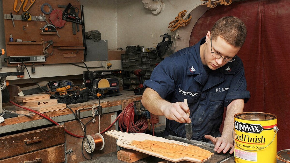 Craftsman applying oil-based wood stain and protective lacquer coating to timber furniture in a wood workshop