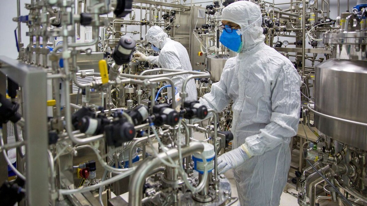 Pharmaceutical cleanroom technicians in full PPE monitoring sterile reaction vessel and sanitary valves